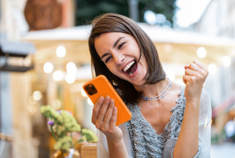 Smiling woman celebrating while using her phone