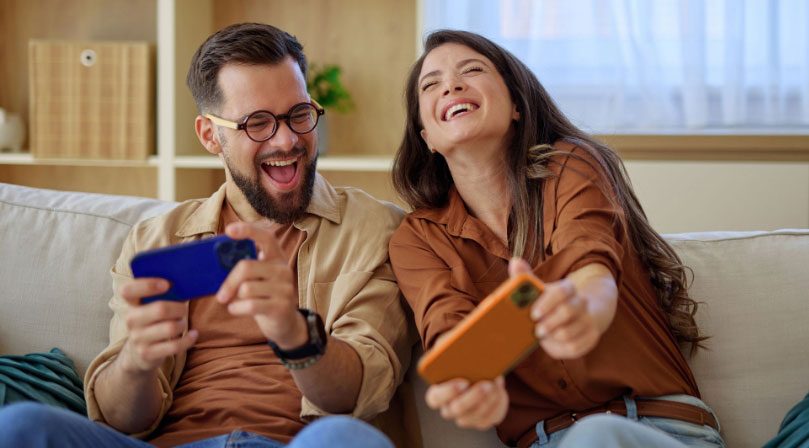 Man and woman smiling and playing games on their smartphones
